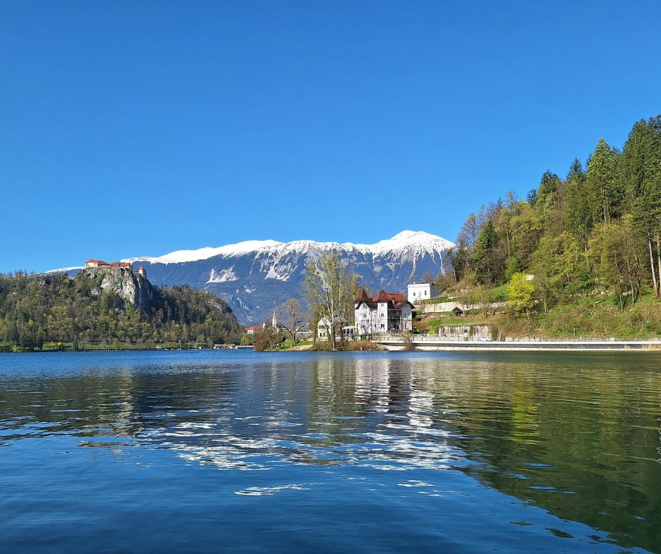 The still lake is surrounded by fresh greenery and snowy peaks in the distance, on an Eastern europe rail holiday