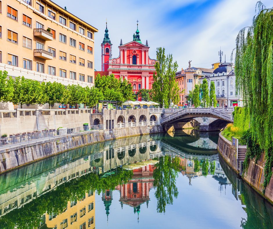 The colourful buildings reflect along the crystal clear canal, on a Slovenian rail holiday