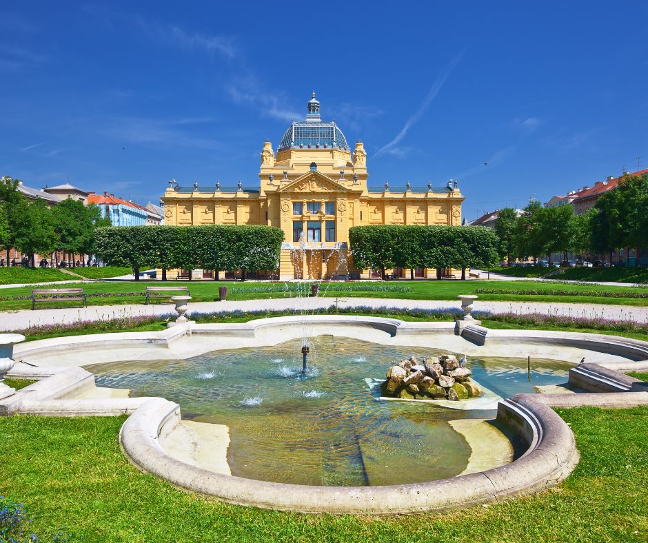 Grand yellow building with classic architecture and a fountain outside, set against a bright sky and capturing the elegance of a croatia rail holiday
